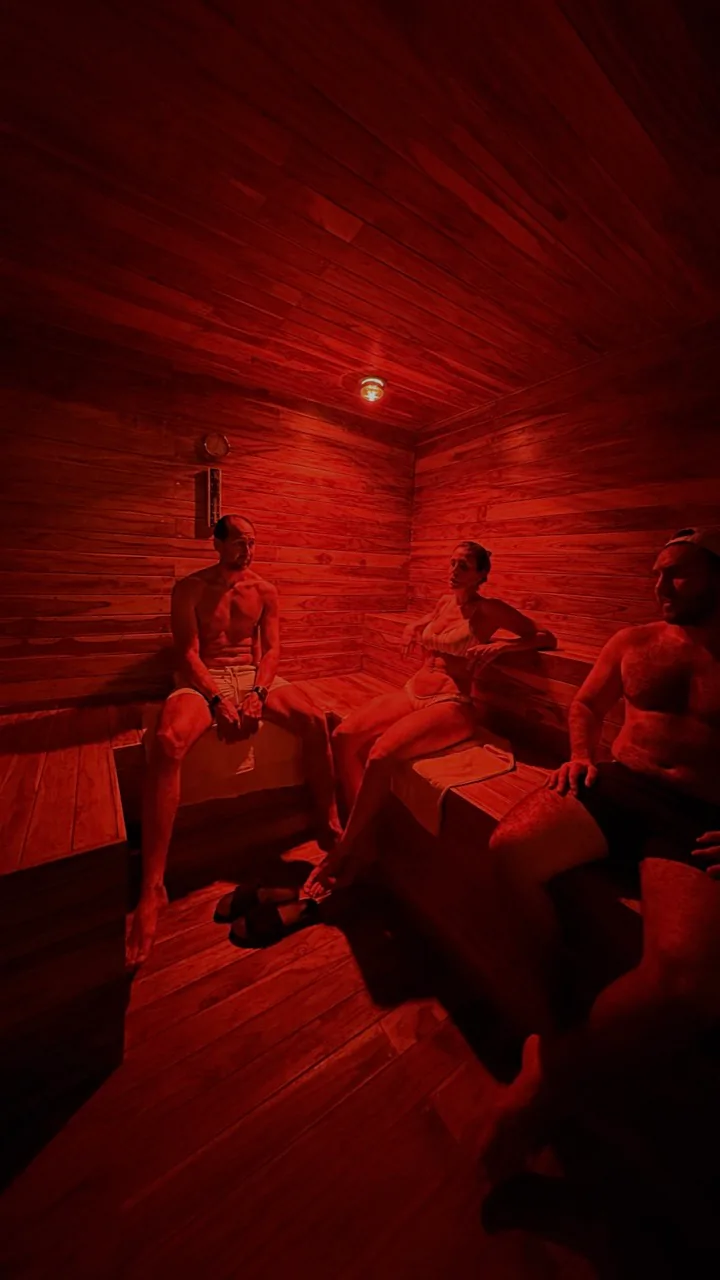 Sauna infrarrojo de madera bajo luz roja con varias personas.